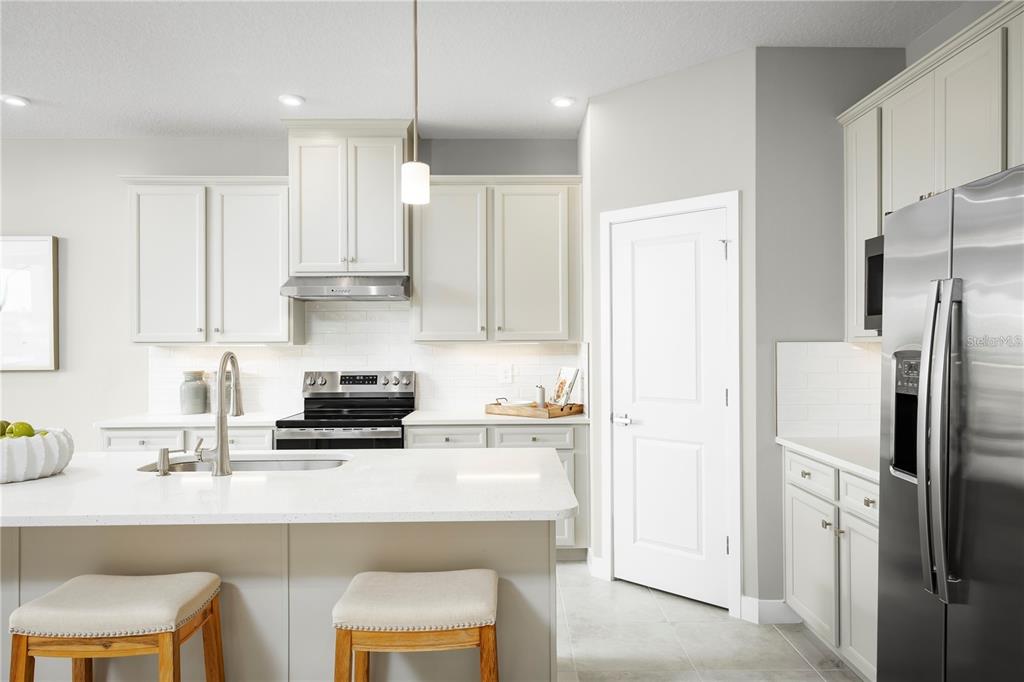A modern kitchen features white cabinetry, a central island with bar stools, and stainless appliances — 20017 GOLDEN GLOW LOOP, VENICE, FL