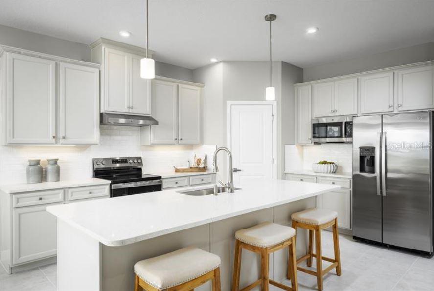 A modern kitchen features white cabinetry, a central island with bar seating, and stainless steel appliances — 20017 GOLDEN GLOW LOOP, VENICE, FL