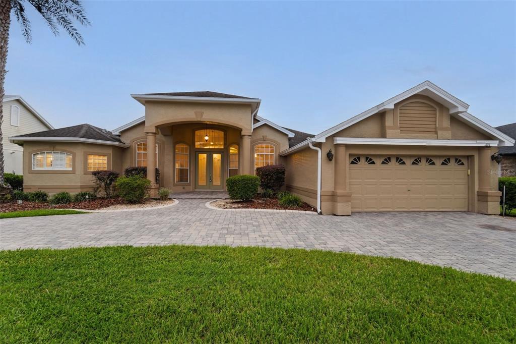 A single-story tan stucco house with a paved driveway, arched entryway, and two-car garage — 1413 CANAL POINT ROAD, LONGWOOD, FL