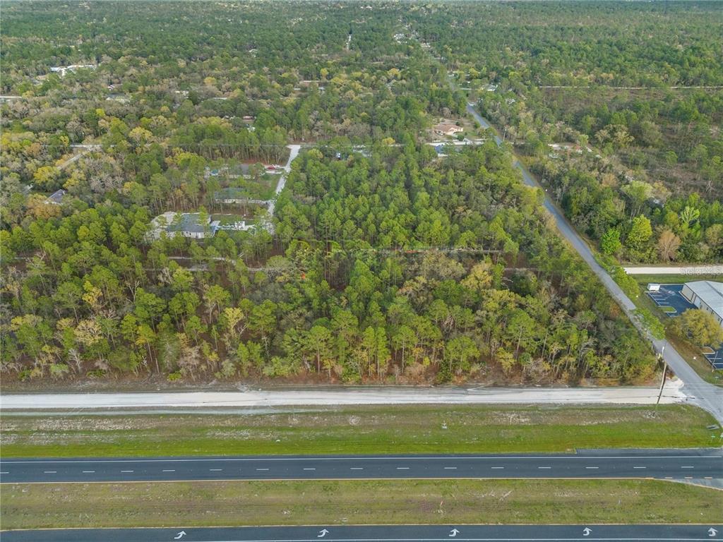An aerial view shows a wooded lot situated between a highway and a residential area — 17416 NICASIO JAY AVENUE, WEEKI WACHEE, FL
