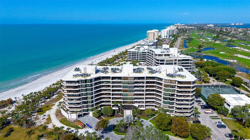 An aerial view shows a multi-story beachfront condominium complex adjacent to a golf course — 535 SANCTUARY DRIVE UNIT A401, LONGBOAT KEY, FL
