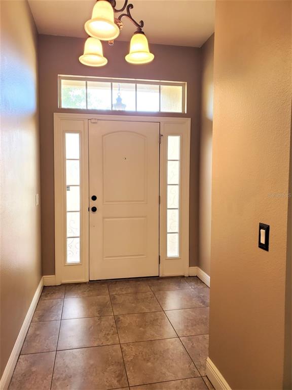 A tiled entryway features a white front door with sidelights, a transom window, and chandelier — 10737 STANDING STONE DRIVE, WIMAUMA, FL