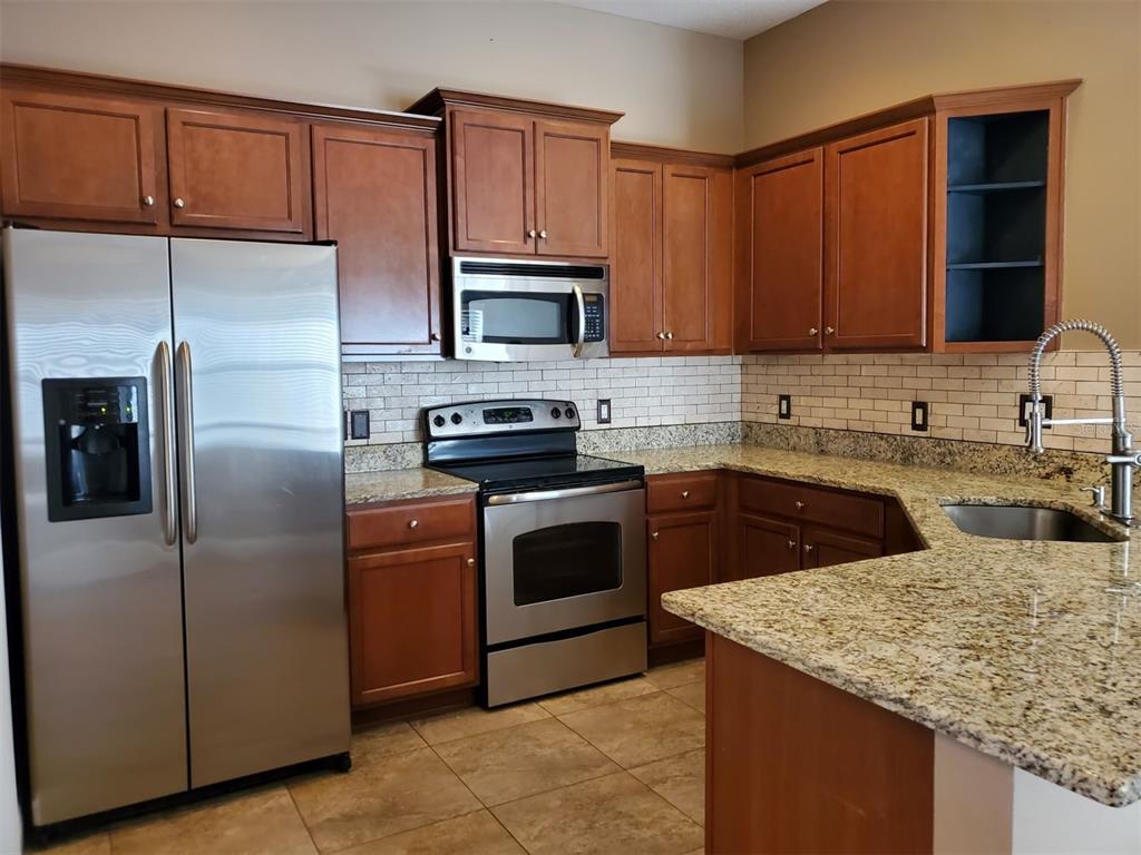 A kitchen with wood cabinets, stainless steel appliances, granite countertops, and a tile backsplash — 10737 STANDING STONE DRIVE, WIMAUMA, FL