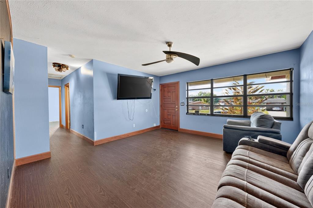 A living room with blue walls, dark wood-look flooring, a ceiling fan, and large windows — 6031 W. RIDGEWOOD AVENUE, ORLANDO, FL