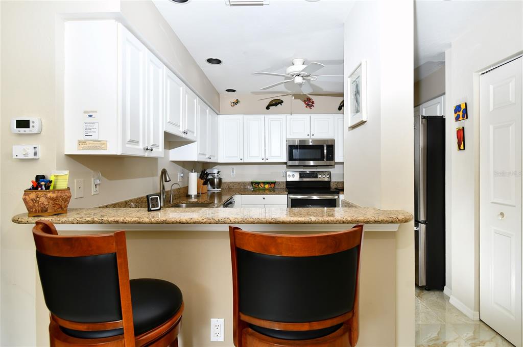 A kitchen with white cabinets, granite countertops, and a breakfast bar with two wooden chairs — 2060 MATECUMBE KEY ROAD UNIT 2402, PUNTA GORDA, FL