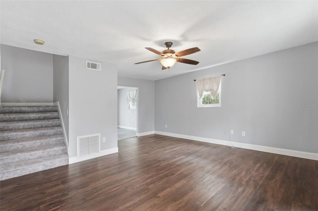 A living room with gray walls, wood-look flooring, a ceiling fan, and carpeted stairs — 41707 ASPEN ST, EUSTIS, FL