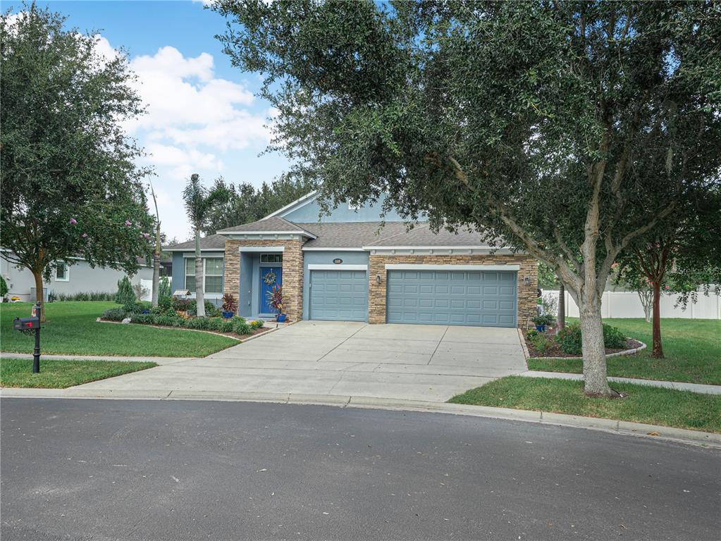 A single-story house with a stone facade, gray siding, and a three-car garage — 112 PECORRI COURT, AUBURNDALE, FL