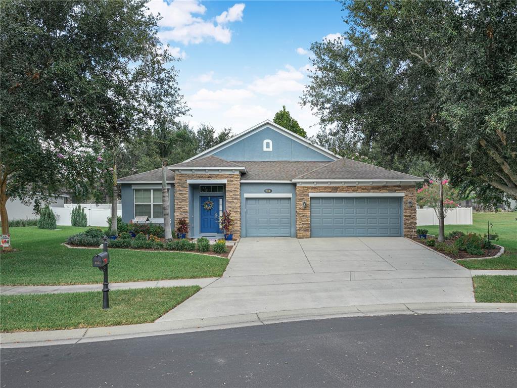 A single-story house with a blue facade, stone accents, and a three-car garage — 112 PECORRI COURT, AUBURNDALE, FL