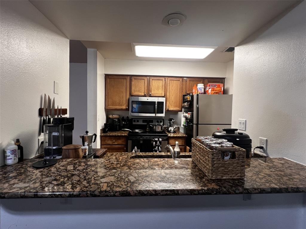 A kitchen features wood cabinets, granite countertops, a stainless steel microwave, and a breakfast bar — 202 RIVERBEND DRIVE UNIT 204, ALTAMONTE SPRINGS, FL