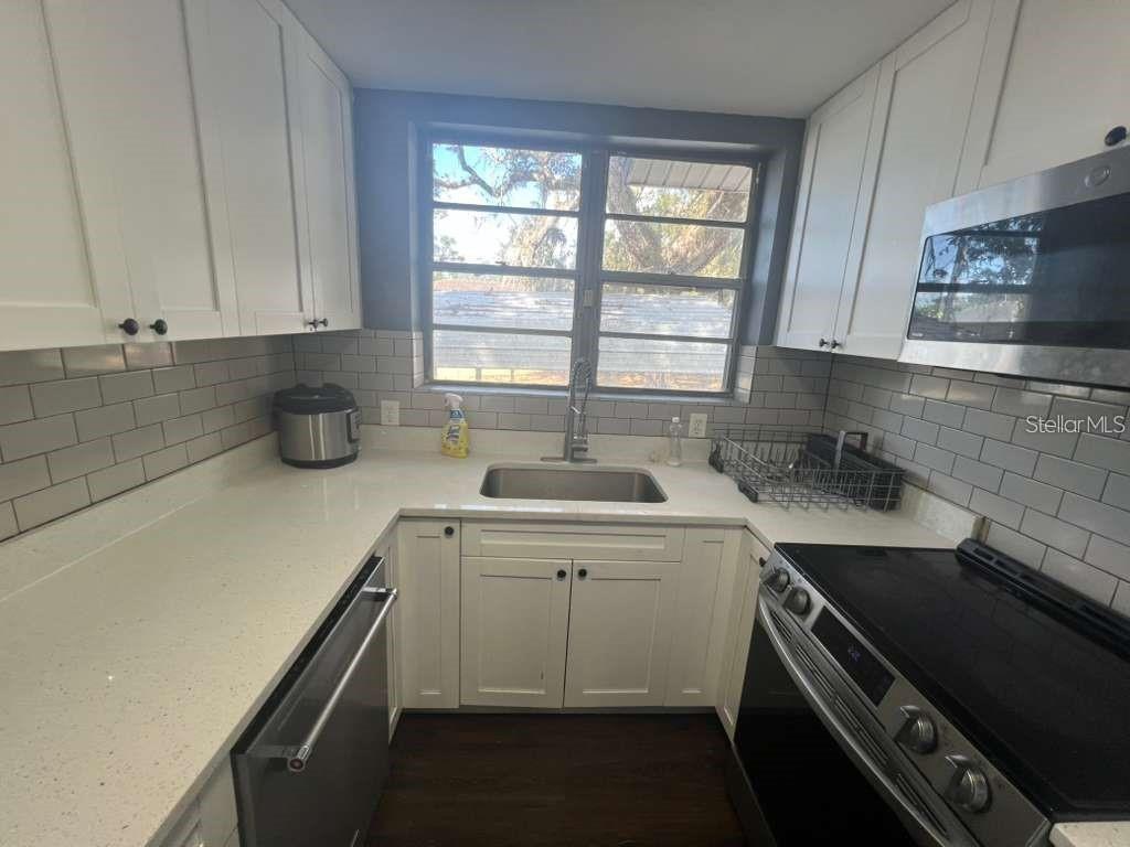 A kitchen features white cabinets, light countertops, a subway tile backsplash, and stainless steel appliances — 2912 CHIPCO STREET, TAMPA, FL