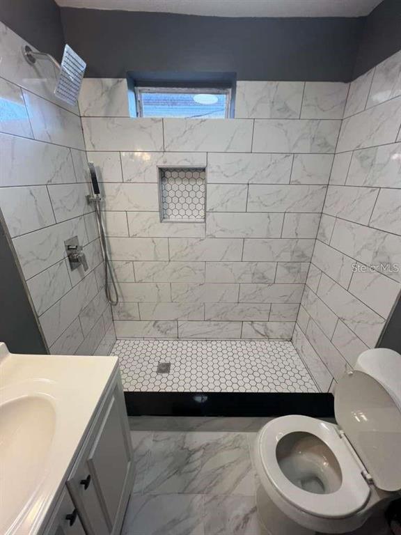A bathroom featuring a walk-in shower with marble-look tile, a niche, and a white toilet — 2912 CHIPCO STREET, TAMPA, FL