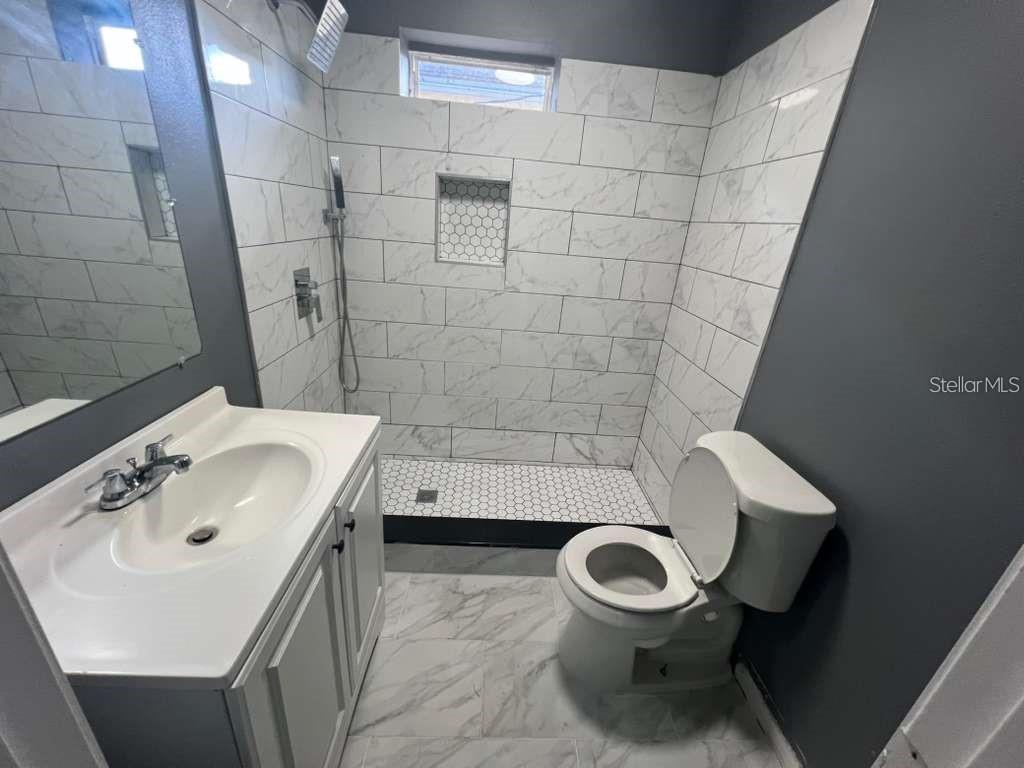A bathroom features a white vanity, a toilet, and a walk-in shower with marble-look tiles — 2912 CHIPCO STREET, TAMPA, FL