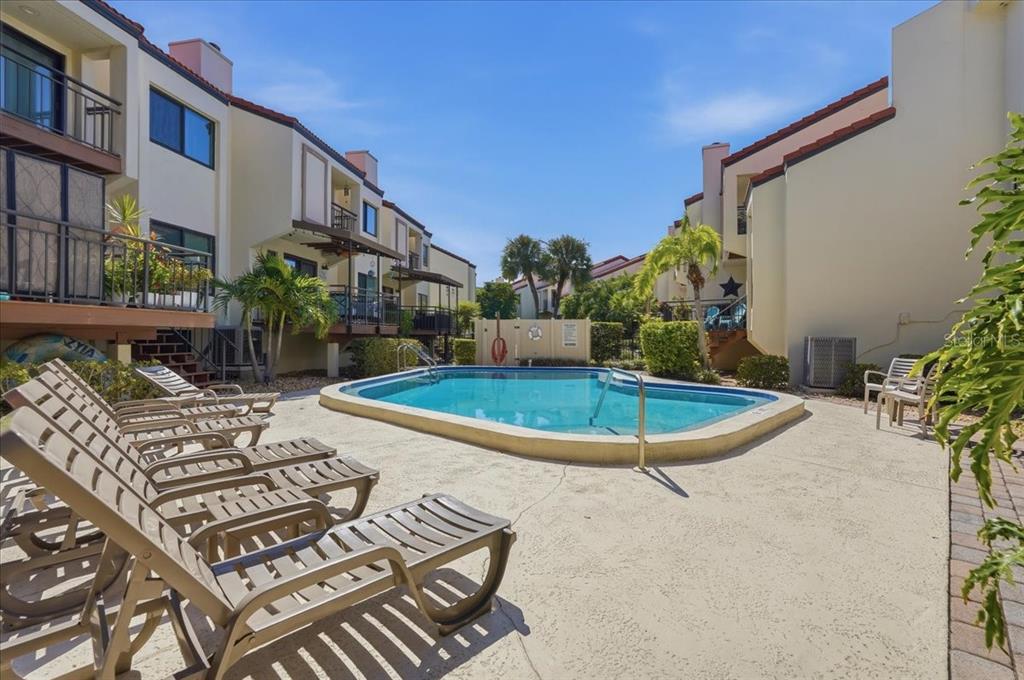 A swimming pool is surrounded by lounge chairs and multi-story apartment buildings under a blue sky — 240 WINDWARD PASSAGE UNIT 702, CLEARWATER, FL