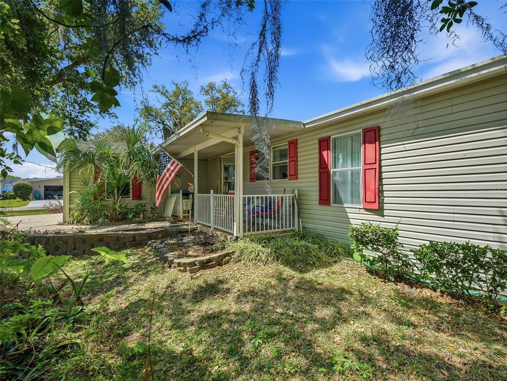A single-story house with light siding, red shutters, and a covered front porch with railings — 387 MARSH LANDING LOOP, OAK HILL, FL