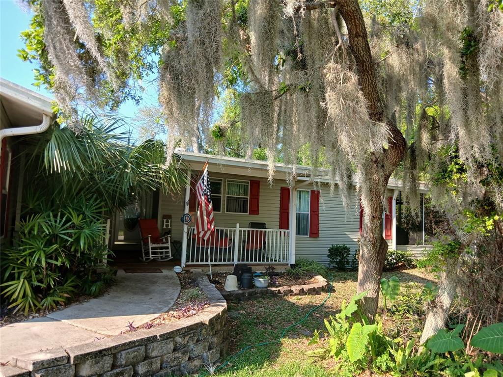 A single-story house with light siding, red shutters, a front porch, and Spanish moss trees — 387 MARSH LANDING LOOP, OAK HILL, FL