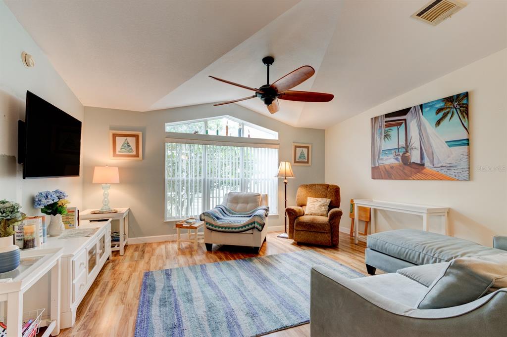 A living room features a vaulted ceiling, wood-look flooring, a ceiling fan, and a large window — 387 MARSH LANDING LOOP, OAK HILL, FL