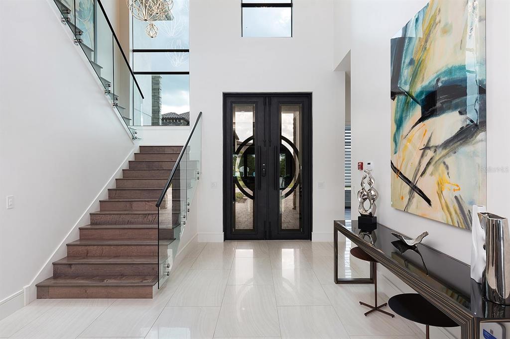 A bright foyer features a glass-railed staircase, large double doors, and a modern console table — 751 GOLDEN BEAR DRIVE, REUNION, FL