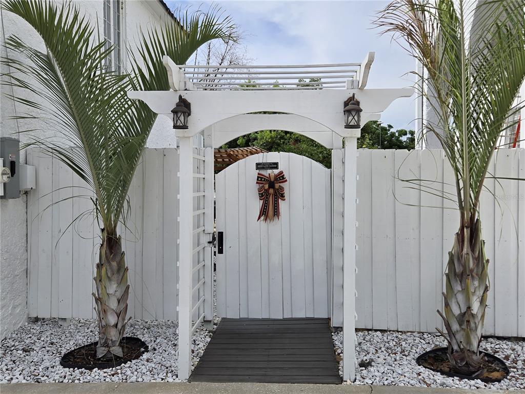 A white wooden arbor and gate stand between two palm trees in front of a fence — 1690 S 10TH STREET UNIT D, HAINES CITY, FL