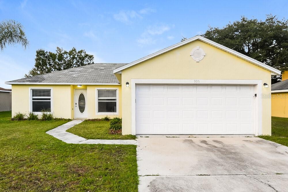 A yellow single-story house features a white garage door, a front entrance, and a concrete driveway — 905 LOUVRE COURT, KISSIMMEE, FL