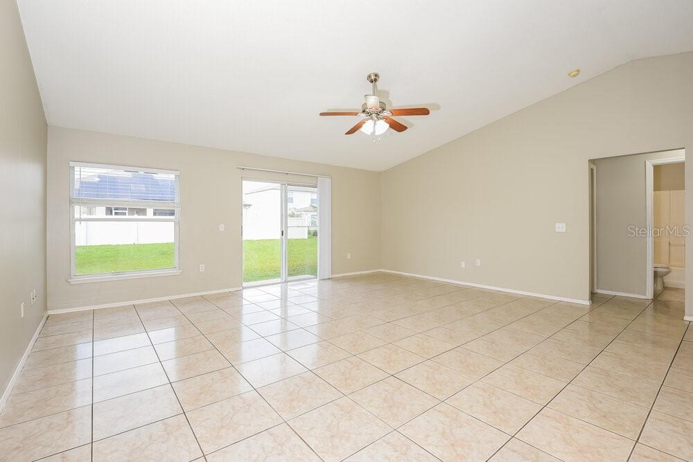 An empty living room features beige tile flooring, vaulted ceilings, and a sliding glass door — 905 LOUVRE COURT, KISSIMMEE, FL