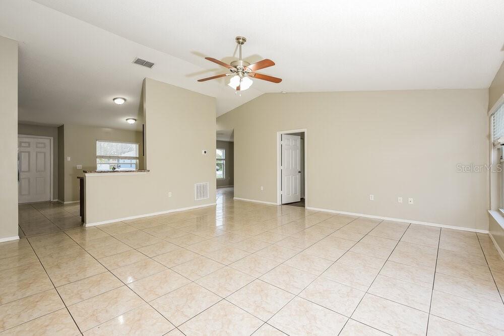 A spacious living room features light-colored tile flooring, a vaulted ceiling, and a ceiling fan — 905 LOUVRE COURT, KISSIMMEE, FL