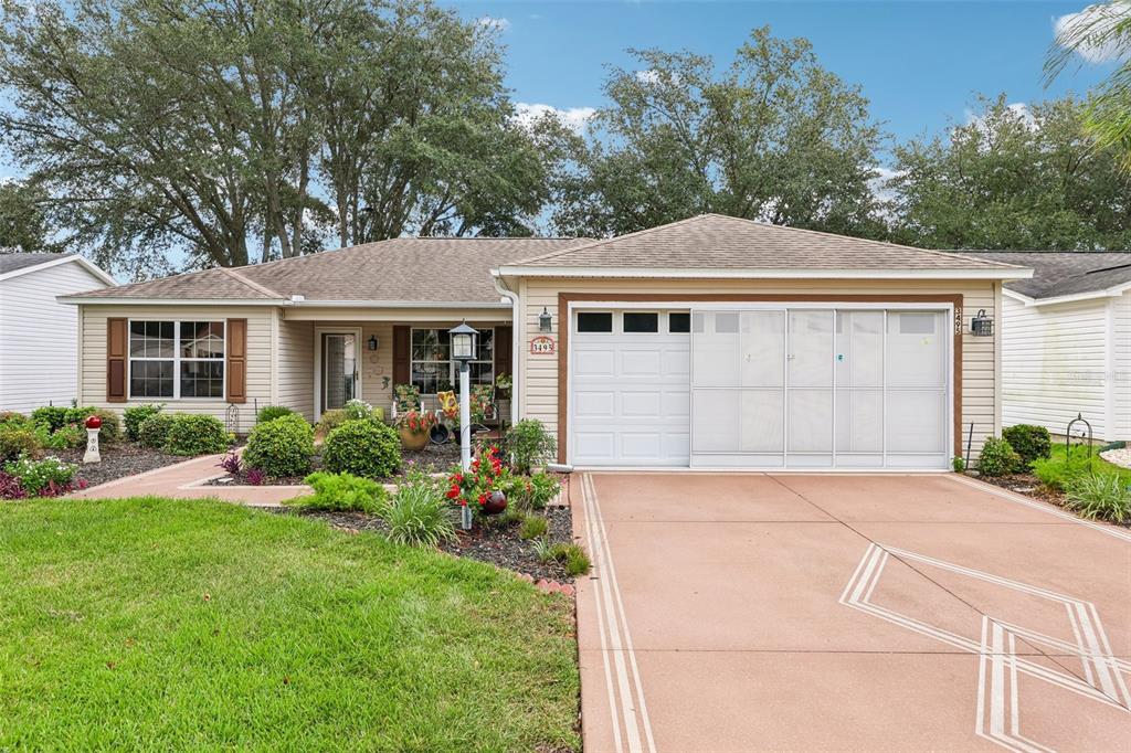 A beige house exterior features a covered porch with two chairs and potted plants — 3495 AUBURNDALE AVENUE, THE VILLAGES, FL