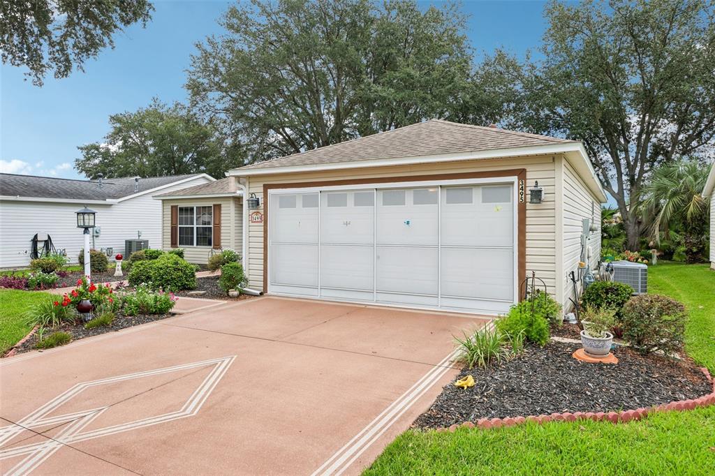 A beige house exterior features a white two-car garage door and a painted concrete driveway — 3495 AUBURNDALE AVENUE, THE VILLAGES, FL