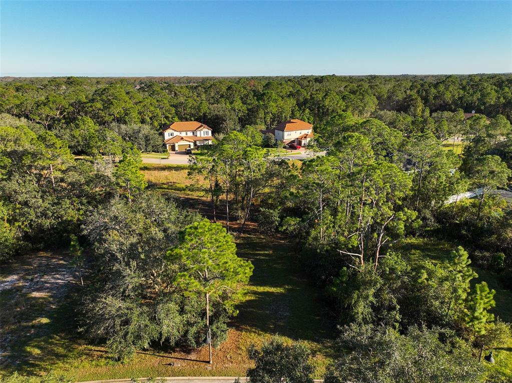 An aerial view shows a vacant, wooded residential lot situated between two large suburban houses — 7180 OAK GLEN TRL, ST CLOUD, FL