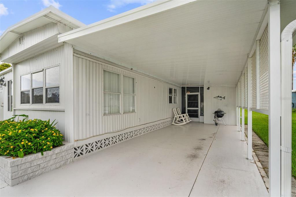A covered carport area with a concrete floor, white siding, and a white rocking chair — 136 LAKEVIEW DR. DRIVE, PALMETTO, FL
