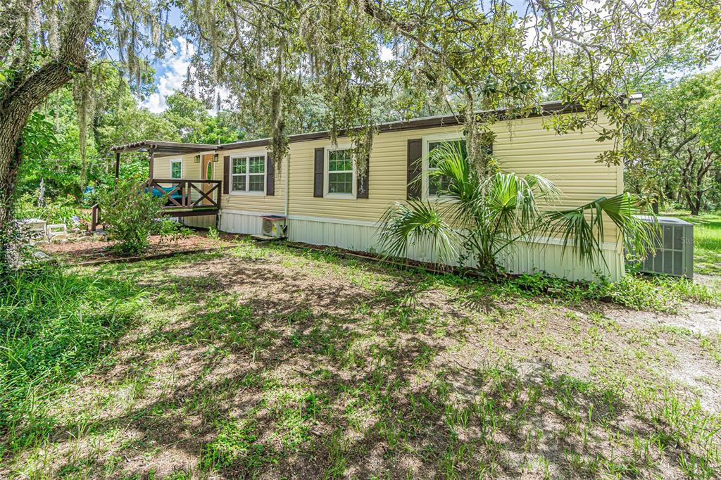 A single-story manufactured home with light yellow siding, a wooden deck, and surrounding trees — 11420 ENGLISH WALNUT STREET, HUDSON, FL