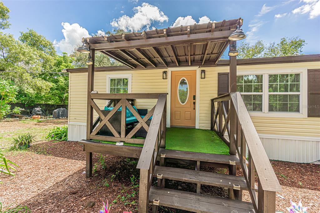 A mobile home exterior features a wooden porch with a pergola and a tan door — 11420 ENGLISH WALNUT STREET, HUDSON, FL