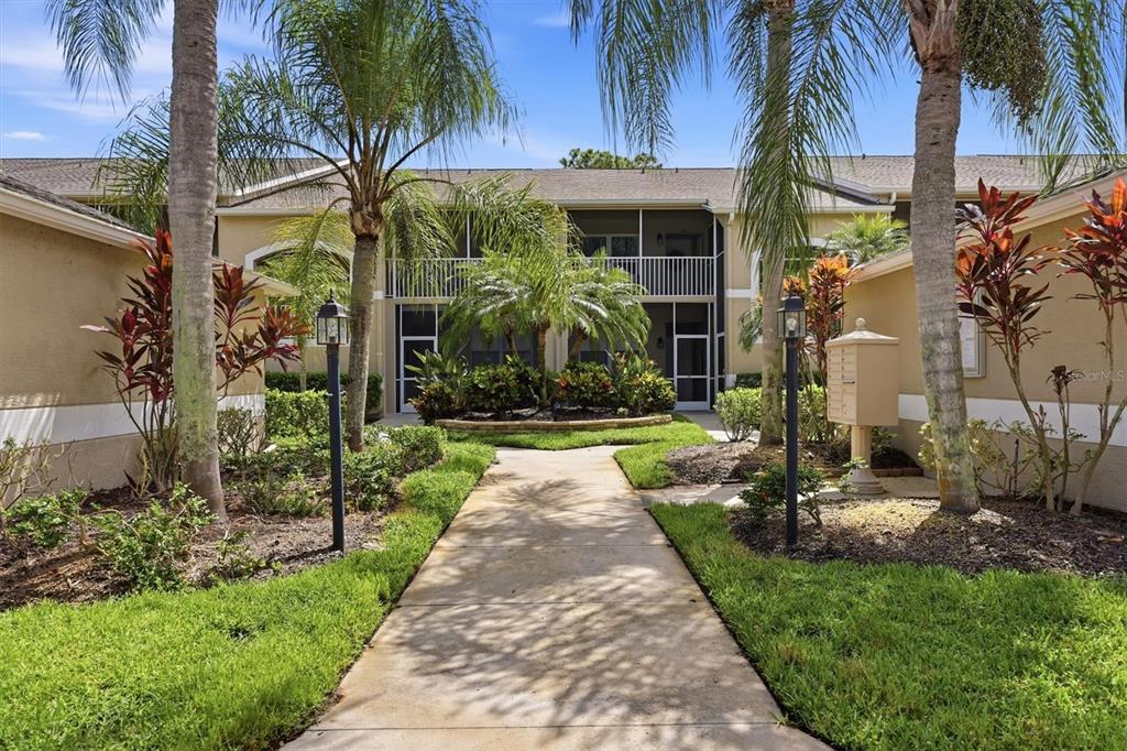A concrete walkway leads to the entrance of a two-story apartment building with palm trees — 5221 MAHOGANY RUN AVENUE UNIT 224, SARASOTA, FL