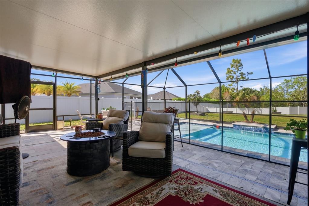 A covered patio with wicker chairs and a fire pit overlooks a screened-in swimming pool — 26 NOAH BOULEVARD, FLAGLER BEACH, FL