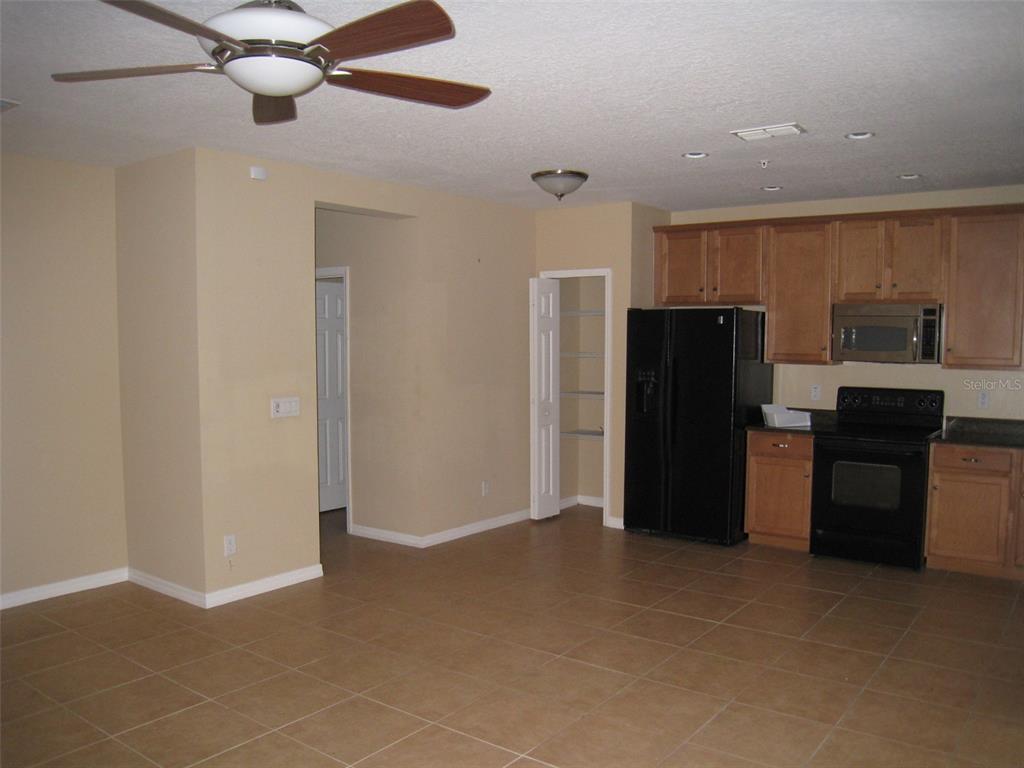 A kitchen and dining area with tan tile floors, light wood cabinets, and black appliances — 9663 BISCOTTI AVENUE, ORLANDO, FL