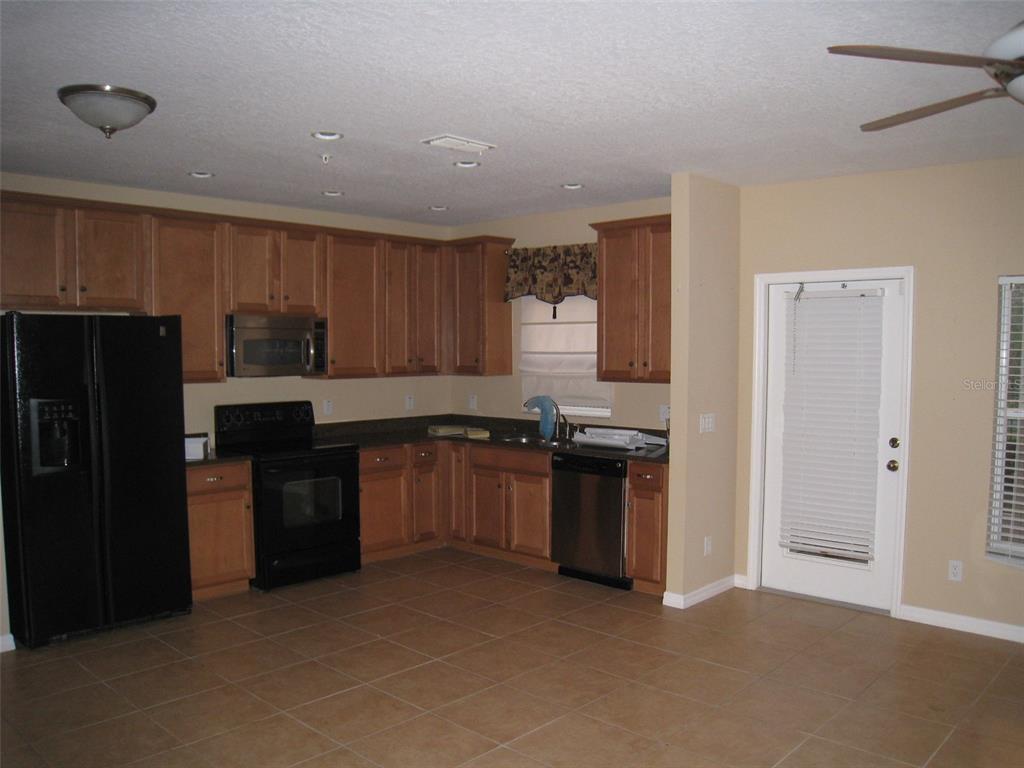 A kitchen with wood cabinets, black appliances, a stainless steel dishwasher, and tan tile flooring — 9663 BISCOTTI AVENUE, ORLANDO, FL