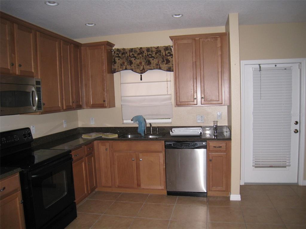 A kitchen features wood cabinets, stainless steel appliances, dark countertops, and tile flooring — 9663 BISCOTTI AVENUE, ORLANDO, FL