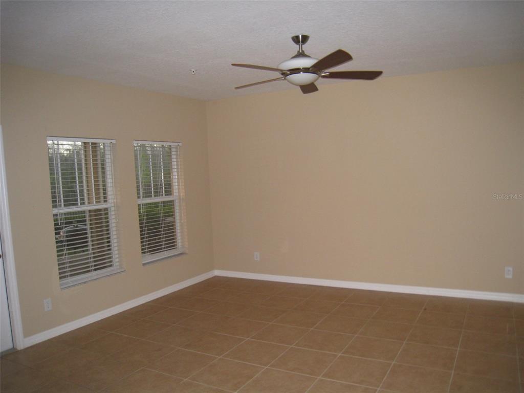 An empty room with beige walls, tile flooring, two windows with blinds, and a ceiling fan — 9663 BISCOTTI AVENUE, ORLANDO, FL