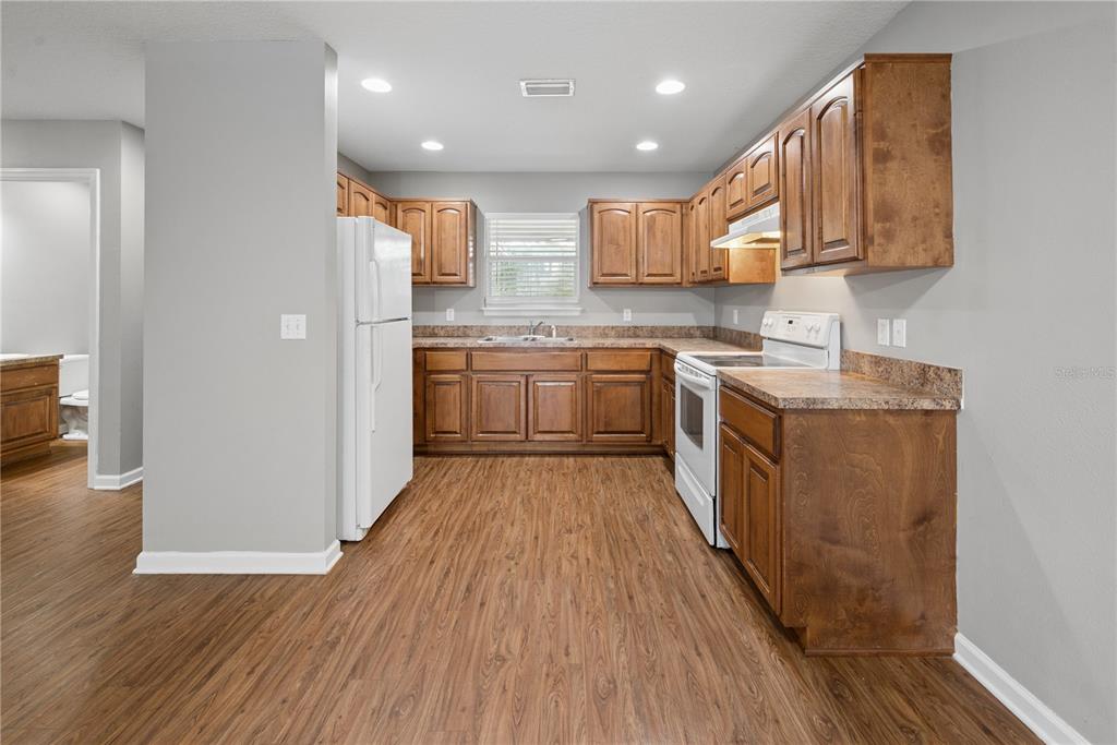 A kitchen with wood cabinets, laminate countertops, white appliances, and wood-look flooring — 226 BRADFORD DRIVE, STARKE, FL