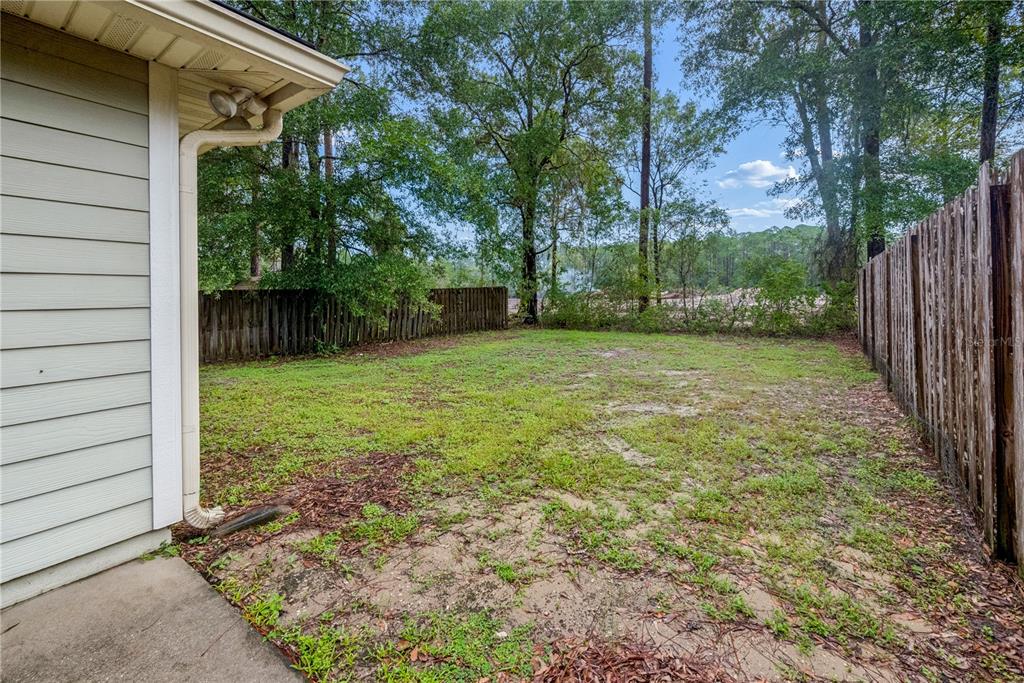 A grassy backyard area enclosed by wooden fences next to the side of a house — 226 BRADFORD DRIVE, STARKE, FL