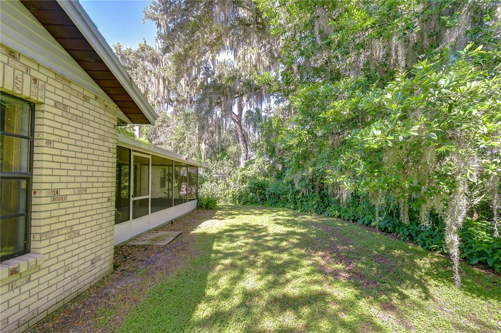 A brick house exterior features a screened-in porch overlooking a grassy backyard with large trees — 716 WESTWOOD DRIVE, BRANDON, FL