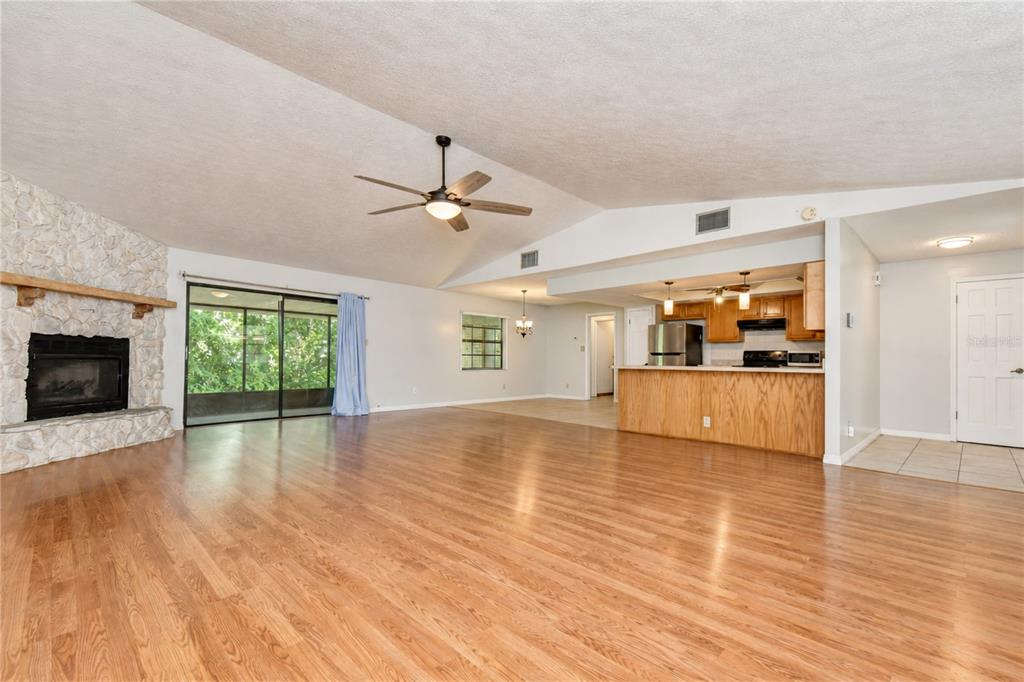 A spacious living room with hardwood floors, a stone fireplace, and an open kitchen area — 716 WESTWOOD DRIVE, BRANDON, FL