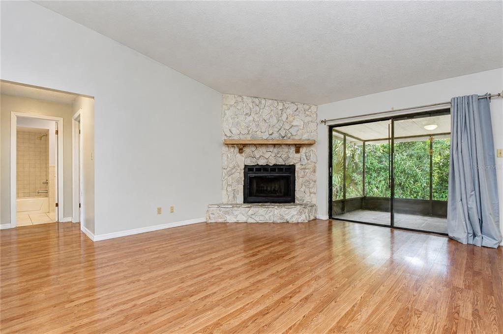 A living room with wood-look flooring, a corner stone fireplace, and sliding glass doors — 716 WESTWOOD DRIVE, BRANDON, FL