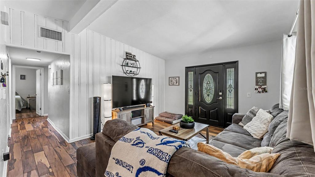 A living room features wood-look flooring, white vertical paneling, a dark front door, and furniture — 680 SUNSET DRIVE, BARTOW, FL