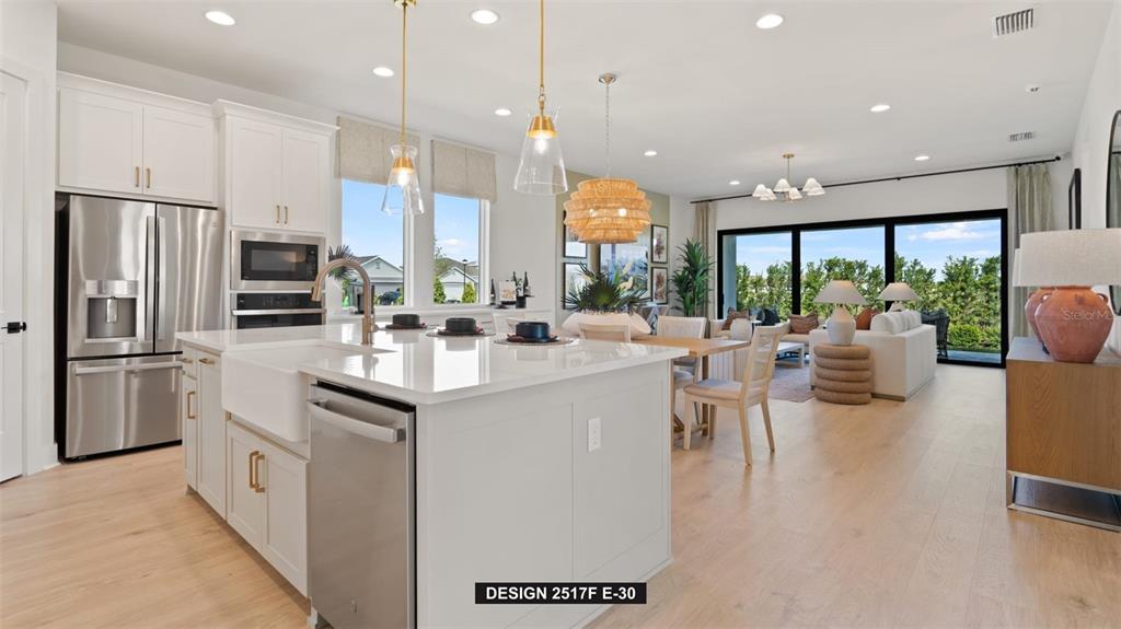 A modern kitchen with a large island and white cabinets opens into a living area — 9531 SANDY SHORES STREET, PARRISH, FL
