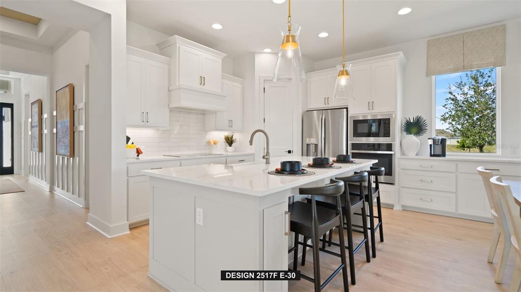 A modern white kitchen features a large center island, pendant lighting, and stainless steel appliances — 9531 SANDY SHORES STREET, PARRISH, FL