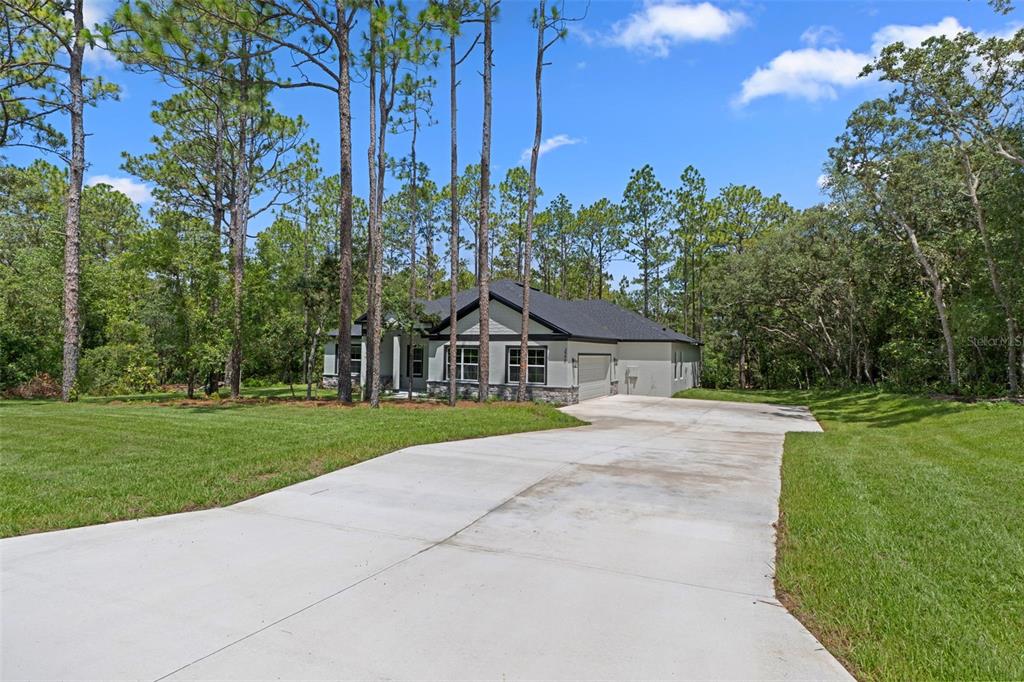 A single-story house with a concrete driveway sits on a wooded lot under a blue sky — 3946 N LONGVALLEY ROAD, HERNANDO, FL