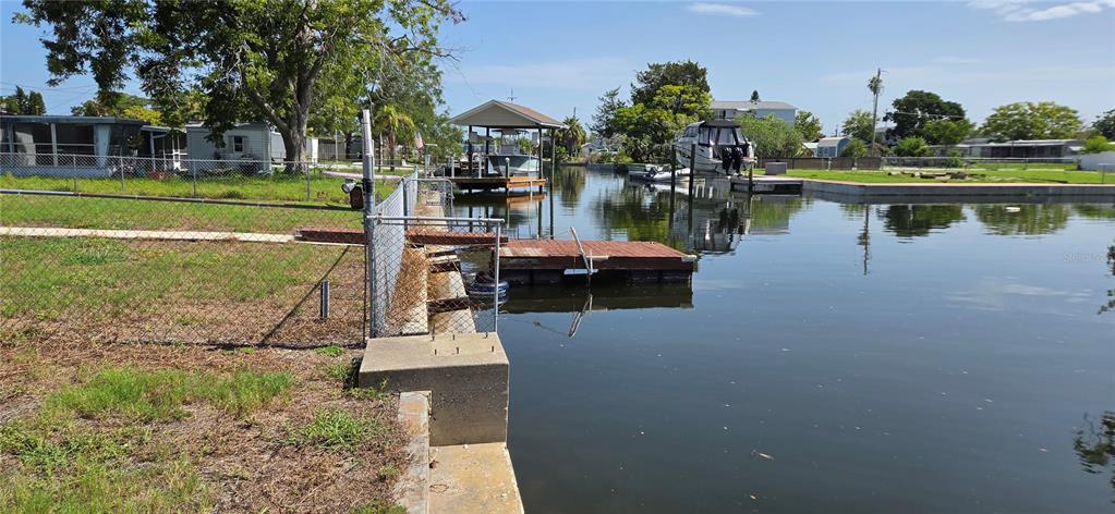 A grassy waterfront lot features a chain-link fence, a concrete seawall, and a wooden dock — 13320 CAROL DRIVE, HUDSON, FL