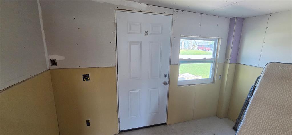 An unfinished room features drywall, a white exterior door, a window, and yellow wall panels — 13320 CAROL DRIVE, HUDSON, FL