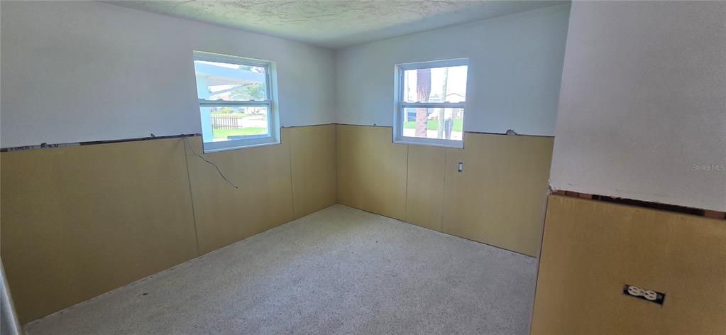 An unfinished room features bare concrete floors, exposed wall panels, and two windows — 13320 CAROL DRIVE, HUDSON, FL