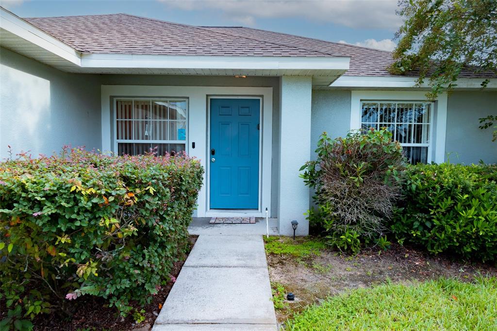 The exterior of a house features a blue front door, a concrete walkway, and landscaping — 128 PINE CONE DRIVE, DAVENPORT, FL
